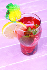 Glass of cold berry cocktail with lemon on wooden background
