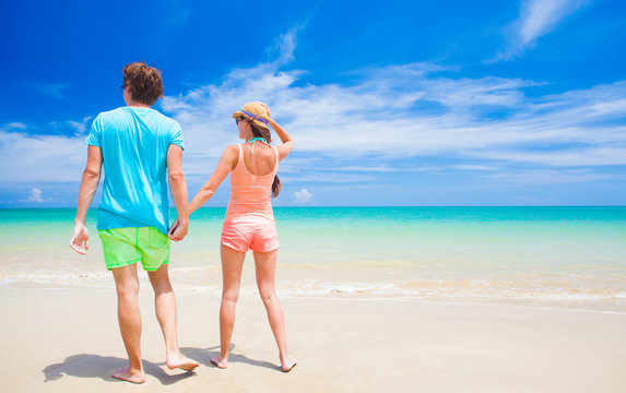 back view of happy young couple holding hands on tropical beach