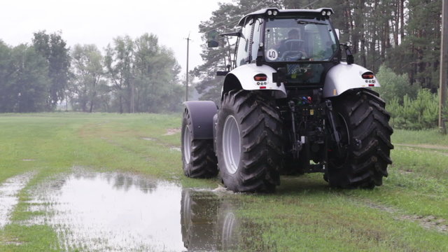 gray tractor rides on the green field on a background of forest 