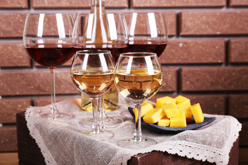 Glasses of wine and cheese on table on brick wall background