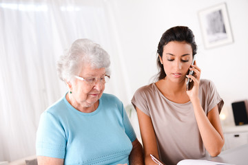 young woman helping old person for paperwork and telephone call
