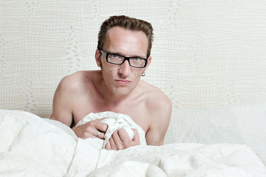 Irritated skinny naked man with angry face sitting in the bed
