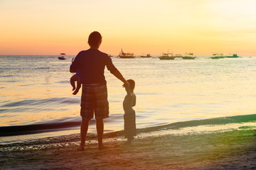 Fototapeta premium Father and kids silhouettes on the beach at sunset