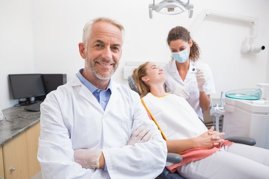 Dentist smiling at camera with assistant and patient behind