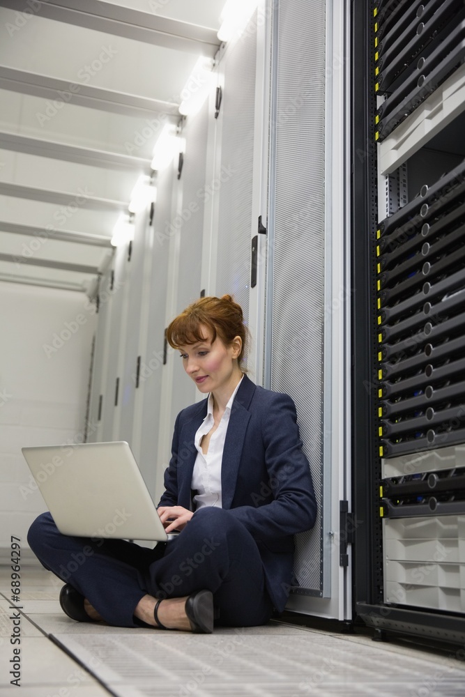 Poster technician sitting on floor beside server tower using laptop