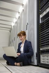 Technician sitting on floor beside server tower using laptop