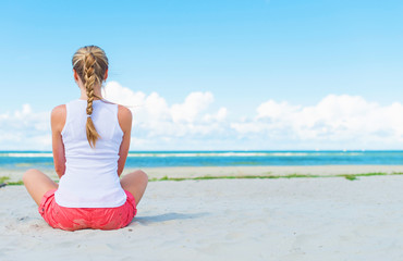 Fototapeta na wymiar Pigtailed girl sitting on the beach and meditating.