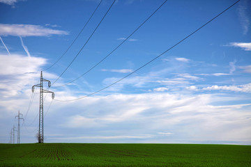 Fototapeta na wymiar Power line in the middle of a green field with blue sky