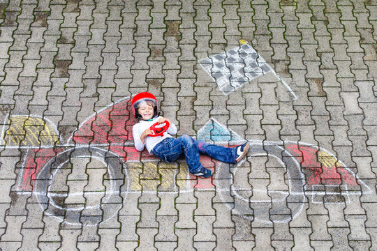Little boy having fun with race car picture drawing with chalk