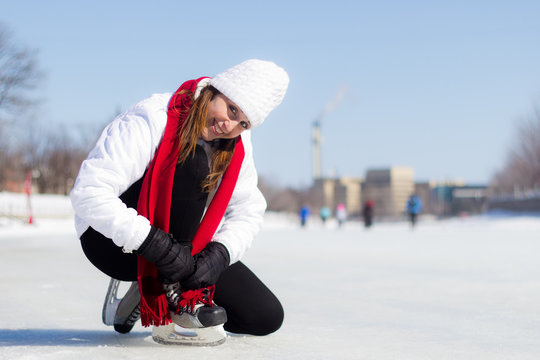 Happy young woman tying her ice skates in winter