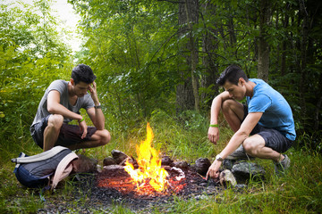 Two young men camping next to burning campfire