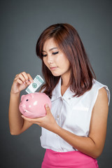 Fototapeta na wymiar Beautiful Asian girl put a bill to pink pig money box