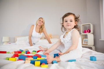 Obraz na płótnie Canvas Mother and daughter playing with building blocks on bed