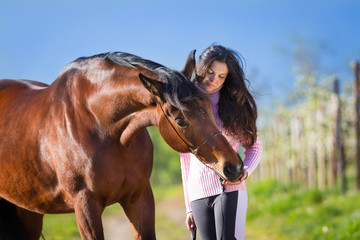 Young beautiful girl standing with a horse in field