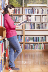 Smiling young student reading a book in a library