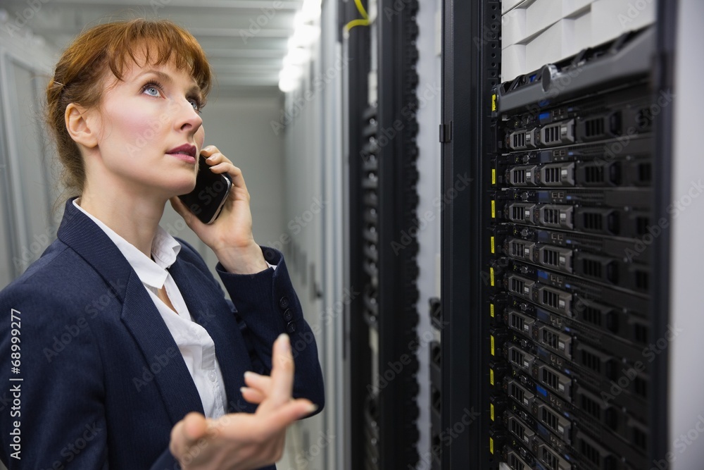Poster pretty technician talking on phone while looking at server