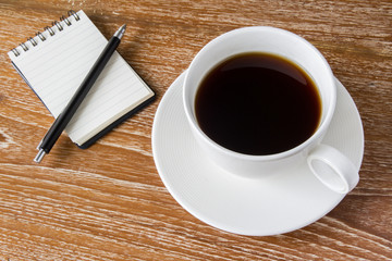 Cup of coffee on wooden table with notebook