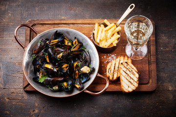Mussels in copper cooking dish and french fries on dark wooden b