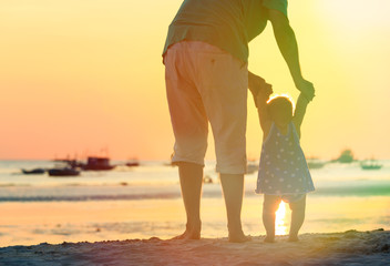 father and little daughter walking on sunset beach