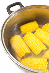 Boiled corn in metal pot on white