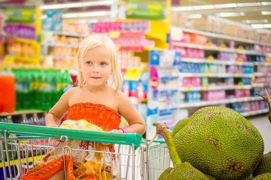 Adorable girl in shopping cart looks at giant jack fruits on box