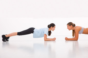 Obraz na płótnie Canvas Two happy young woman doing push-ups in gym