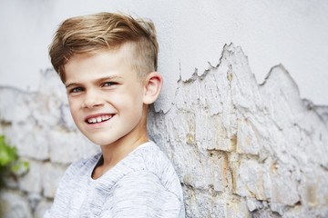 Portrait of young boy leaning against wall.