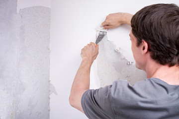 Heimwerker kratzt Tapete von der Wand