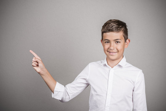 Happy teenager pointing at blank copy space grey background 