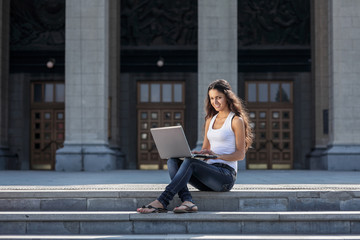 A young woman with a laptop sitting on the stairs, near the univ