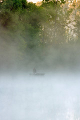 Lonely fisherman in foggy lake