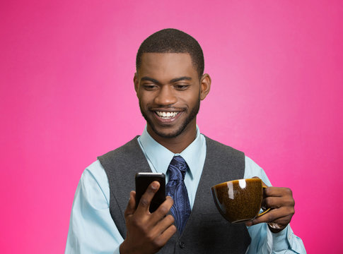 Smiling businessman reading news on mobile, drinking tea