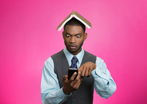 Shocked man holding mobile, book over head pink background 