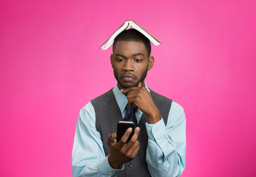 Man holding mobile phone, book over head, pink background 