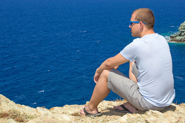 man sitting on rocky cliff on sea coast