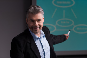 Mature trainer pointing at screen with presentation.