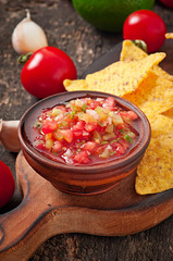 Mexican nacho chips and salsa dip in bowl on wooden background