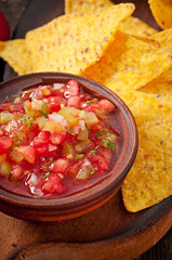 Mexican nacho chips and salsa dip in bowl on wooden background
