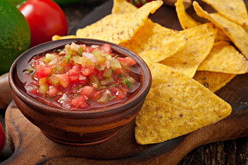 Mexican nacho chips and salsa dip in bowl on wooden background