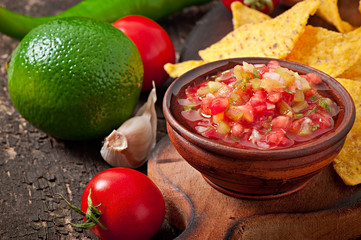 Mexican nacho chips and salsa dip in bowl on wooden background