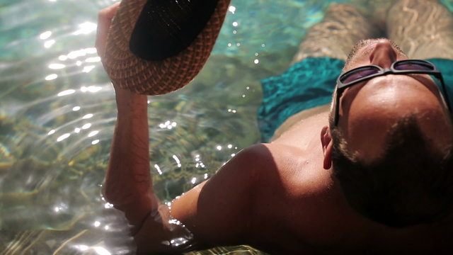 Young man sunbathing in the swimming pool on hot summer day