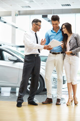 Young Couple Signing a Contract in Car Showroom.