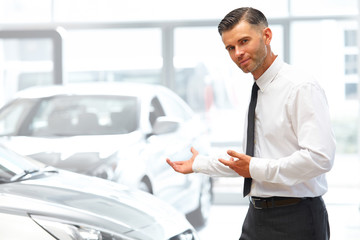 Salesman Standing at the Car Showroom and Showing New Cars