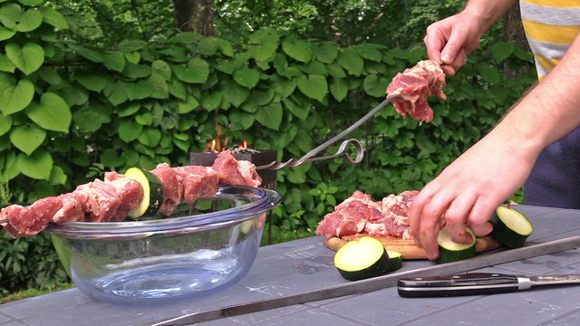 Man hand put raw meat and courgette vegetable pieces on skewer