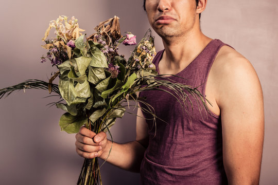 Young man holding bouquet of dead flowers
