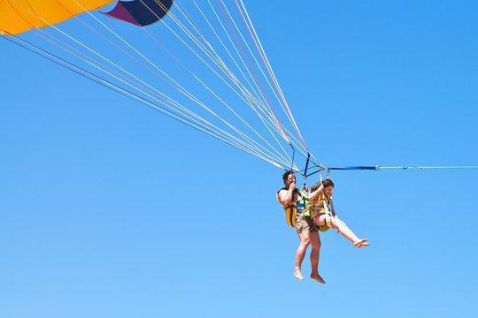 man and girl parasailing on parachute in blue sky