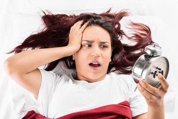 Girl lying on a bed looking at the alarm clock