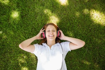 Pretty redhead lying on grass listening to music