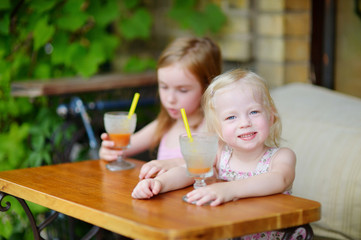 Obraz na płótnie Canvas Two sisters drinking juice in outdoor cafe