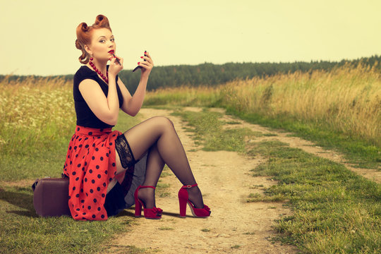 woman  sitting on the side of a rural road painting lipstick.